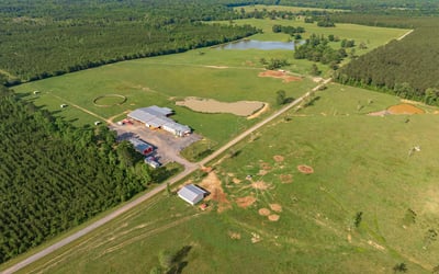 Expansive countryside property featuring vast open fields, wooded areas, and a tranquil pond, ideal for various uses.