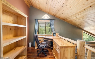Dedicated loft office featuring built-in shelving, wood finishes, and natural light perfect for a quiet workspace within this Prescott log home.