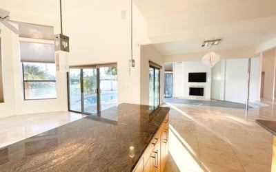 Gourmet kitchen with open flow into living area. Refined pendant fixtures and granite surfaces define this bright, upscale space.