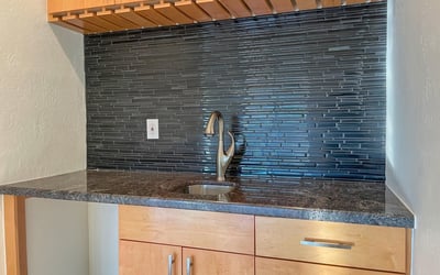Granite counters, warm wood cabinetry, and a glossy backsplash make this wet bar a sophisticated entertaining feature.