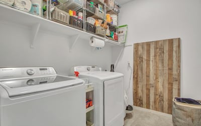 This convenient laundry room includes overhead shelving, full-size appliances, and tile flooring, making chores easy in this Litchfield Park home.