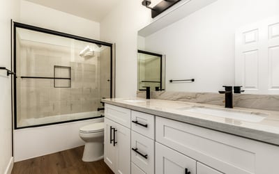 Updated Scottsdale guest bathroom with dual sinks, contemporary cabinetry, and modern black fixtures. The bathroom also includes a glass shower enclosure and elegant finishes that complement the home s remodeled interior.