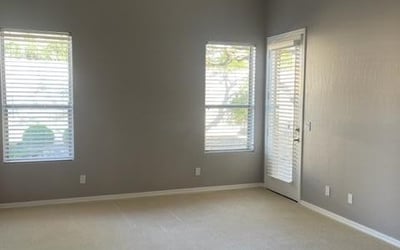 Bright bedroom with large windows, soft carpeting, and ceiling fan. Ideal for restful nights and flexible furniture placement.