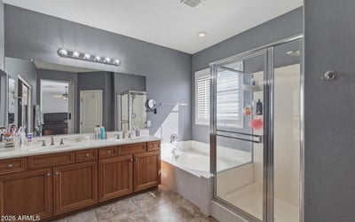 Primary bathroom with dual sinks, wood cabinetry, and bright lighting, providing a functional and stylish space for daily routines.