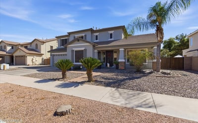 Inviting Queen Creek home exterior featuring desert landscaping, palm trees, stone accents, and a covered entry creating beautiful curb appeal.