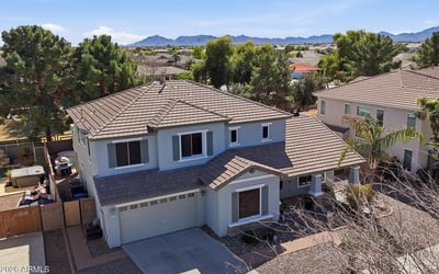 Elevated drone view showing the home's position within the neighborhood with distant mountain scenery and surrounding residential streets in Queen Creek.