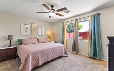 Spacious primary bedroom featuring large window, ceiling fan, and plush carpet creating a relaxing private retreat.