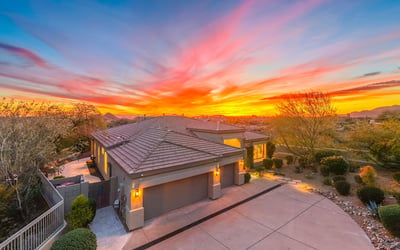 Beautifully maintained Scottsdale home with modern architecture, spacious driveway, and warm exterior lighting set against a vibrant sunset backdrop.