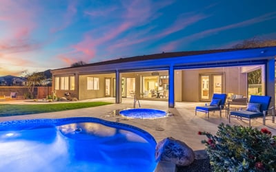 Scottsdale backyard featuring glowing spa, poolside seating, and covered patio, ideal for evening relaxation and entertaining.
