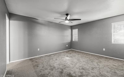 Spacious bedroom with soft carpet, ceiling fan, and neutral tones. This Sun City home provides a relaxing retreat with move-in ready comfort.