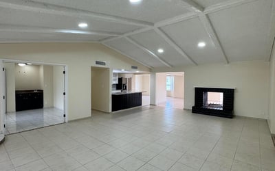 Open living room with dramatic wood-beamed ceilings, tile flooring, and a statement fireplace. The spacious design offers flexibility for entertaining and comfortable daily living.