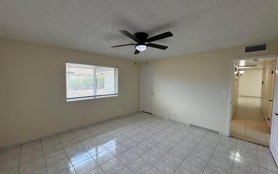 Comfortable guest bedroom featuring neutral finishes, tile flooring, and a ceiling fan. Large windows provide natural light while maintaining a clean, move-in-ready appearance.