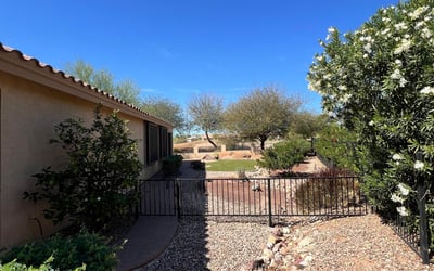 Beautiful side yard featuring flowering shrubs, decorative rock landscaping, gated access, and paver walkways that enhance both privacy and the home's low-maintenance outdoor design.