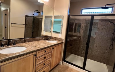 Beautiful primary bath offering dual vanities, abundant cabinetry, upgraded countertops, modern fixtures, and a spacious tiled walk-in shower. A relaxing retreat designed with both comfort and functionality in mind.