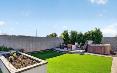 Beautiful backyard featuring artificial turf, raised garden planters, paver hardscaping, and a private hot tub creates a low-maintenance outdoor oasis in Surprise.