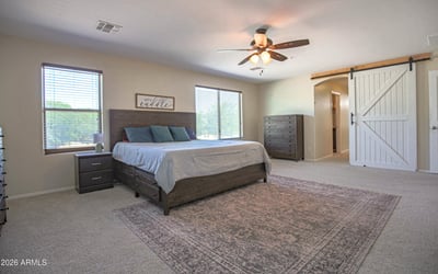 Oversized owner's suite featuring plush carpeting, abundant natural light, ceiling fan, and sliding barn door access to the private en-suite bath. A peaceful retreat in this desirable Waddell home.