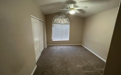 Featuring soft carpeting, a ceiling fan, an arched window, and ample closet space, this inviting bedroom offers flexibility for guests, family, or a home office.
