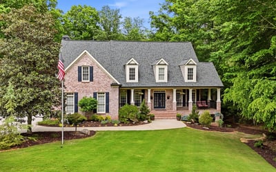 This beautiful home features a welcoming front porch, expansive lawn, and lush surrounding greenery for privacy.