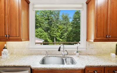 Bright kitchen featuring rich wood cabinetry and a scenic view of lush greenery through a large window.