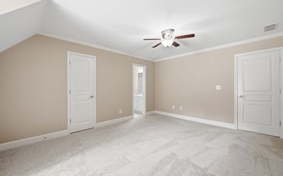 Spacious bedroom featuring soft carpeting, a ceiling fan, and access to a private bath.
