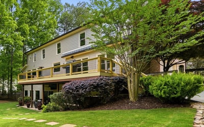 Discover a spacious home with a large deck, surrounded by lush landscaping and vibrant greenery.
