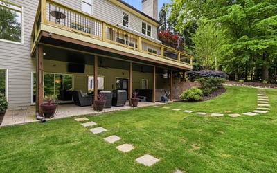 Spacious outdoor living area features a deck overlooking a lush, landscaped yard with stone pathways.
