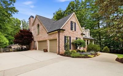 Stunning brick home with a spacious driveway, surrounded by lush landscaping and mature trees.