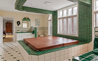 This unique bathroom features a sunken hot tub surrounded by vibrant green tile accents and ample natural light.