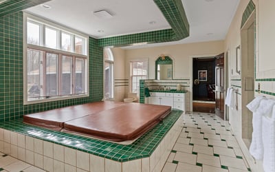 Spacious bathroom featuring a large sunken tub, extensive green tilework, and ample natural light.