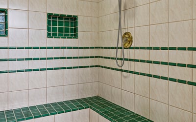 Spacious walk-in shower featuring unique green tile accents and built-in seating for added convenience.