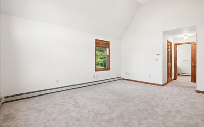 Spacious room with vaulted ceiling, large windows, and neutral carpeting, ready for your personal touch.