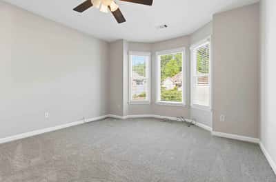 Bright and airy bedroom featuring large windows, plush carpeting, and a ceiling fan for comfort.