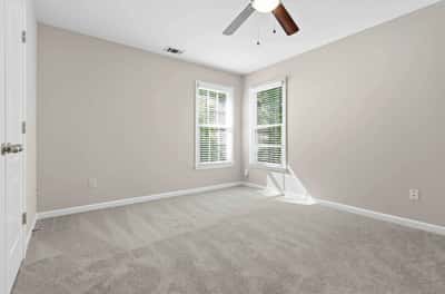 Bright and spacious bedroom featuring ample natural light, new carpeting, and modern ceiling fan for comfort.