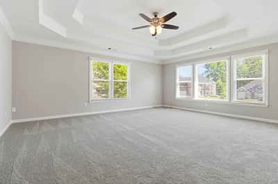 Spacious, light-filled primary bedroom featuring a coffered ceiling and large windows for ample natural light.