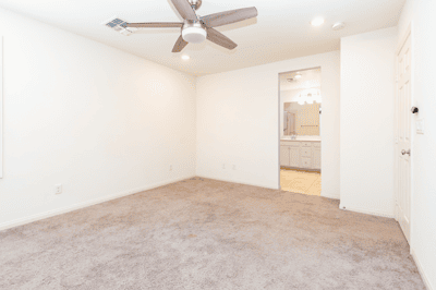 Spacious, versatile room with soft carpeting and a ceiling fan, leading to a modern bathroom.