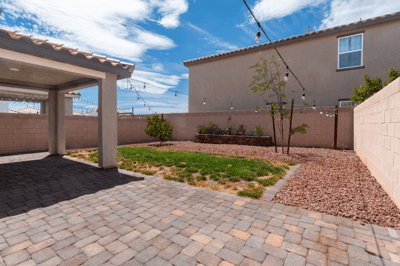 Discover a spacious backyard with a paver patio, decorative plants, and overhead string lights