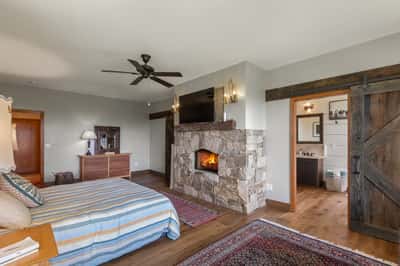 Spacious bedroom featuring a stone fireplace, rustic beams, and direct access to an en-suite bathroom.