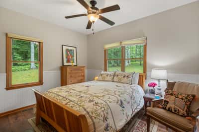 Light-filled bedroom featuring large windows, cozy furnishings, and a tranquil forest view for peaceful living.