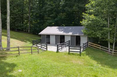This property features a spacious barn surrounded by lush greenery and rustic fencing, ideal for outdoor enthusiasts.