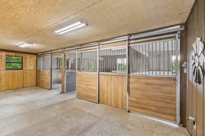 This spacious equestrian facility features multiple stalls, ample lighting, and easy access to outdoor areas.
