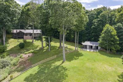 Nestled among lush trees, this property features a spacious home and a quaint outbuilding on rolling land.