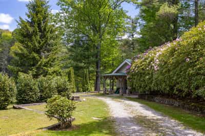 This picturesque property features lush landscaping, a winding gravel drive, and a cozy entrance nestled among the trees.