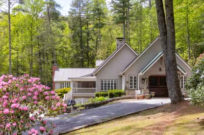 Nestled among lush greenery, this inviting home features a spacious driveway and warm outdoor gathering areas.