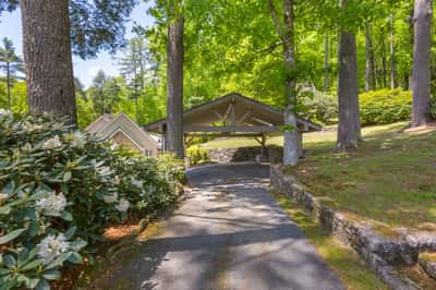 Private driveway leads to a spacious carport nestled among lush trees and vibrant landscaping.