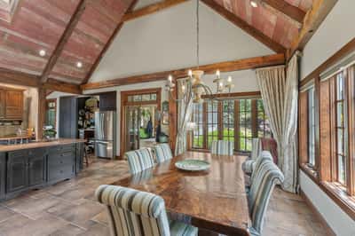 Sunlit dining area with vaulted ceilings, featuring rustic wood beams and large windows overlooking the garden.