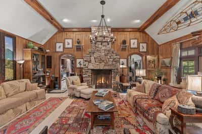 Spacious living area features a stone fireplace, wood paneling, and panoramic windows for natural light.