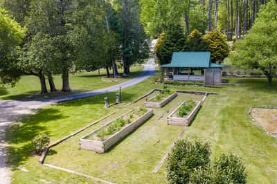 Spacious outdoor space featuring raised garden beds, a cozy gazebo, and lush greenery, ideal for gardening enthusiasts.