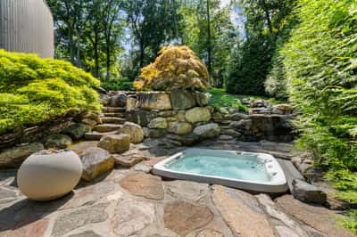 Discover a private outdoor oasis featuring a hot tub surrounded by natural stone and vibrant greenery.