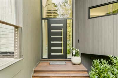 Modern entrance featuring a sleek door and striking wood steps, surrounded by lush greenery.