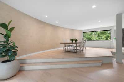 Spacious dining area featuring a unique curved wall and large windows, offering abundant natural light and greenery views.